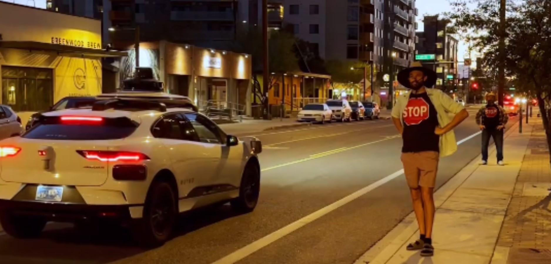Мужчина в майке с изображением знака STOP оснанавливает беспилотные машины на улице